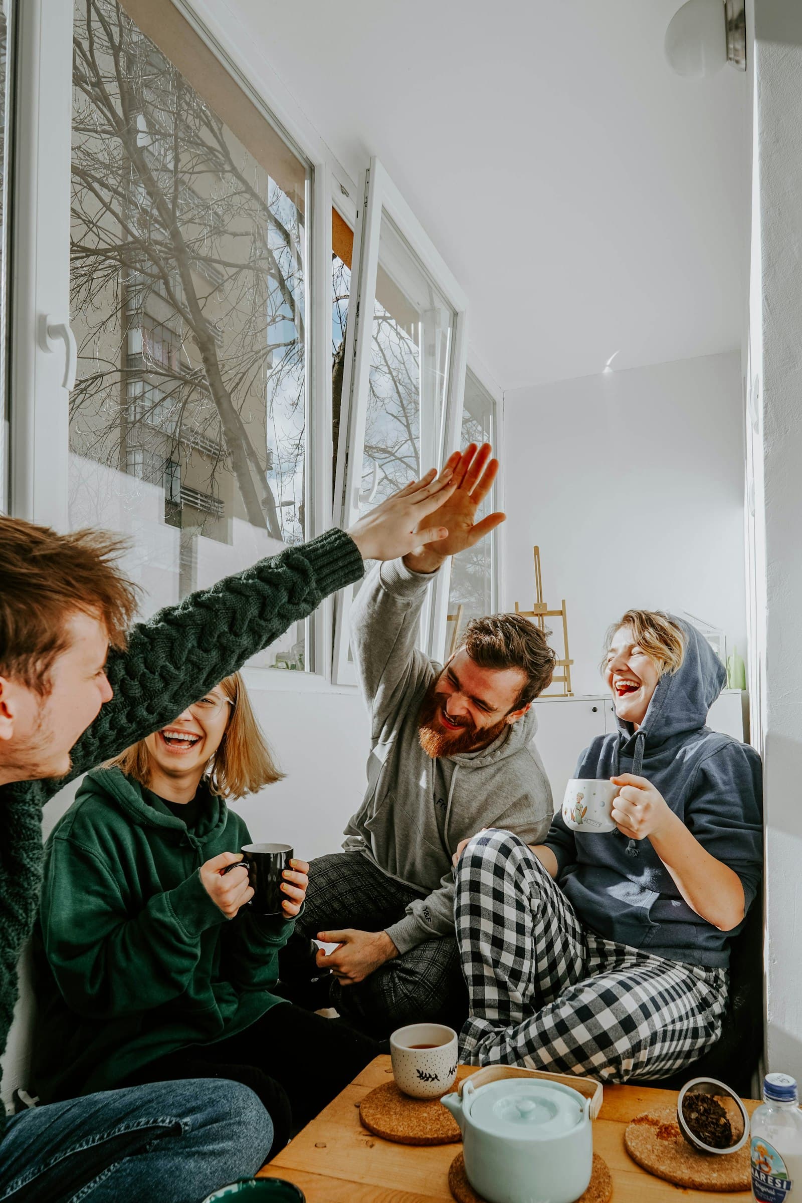 Four young friends laughing together around a small table, mid-conversation