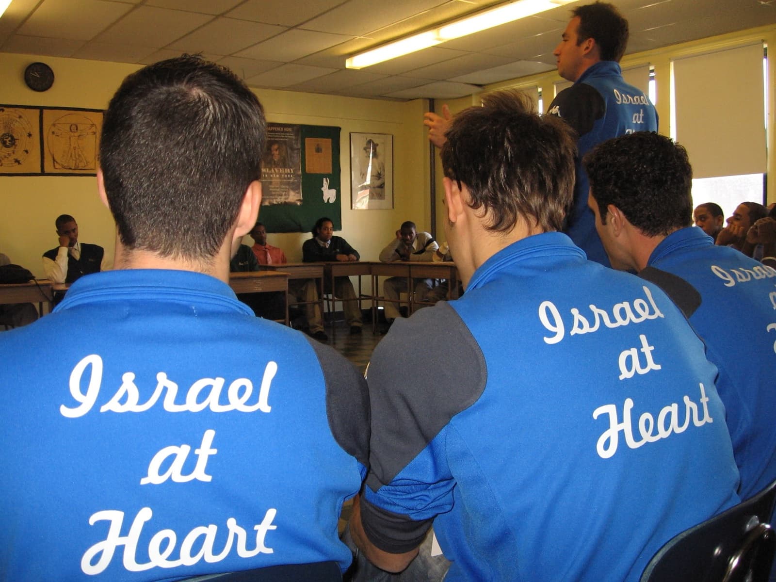 Israel at Heart players in team jackets sitting and talking with students in a college classroom.