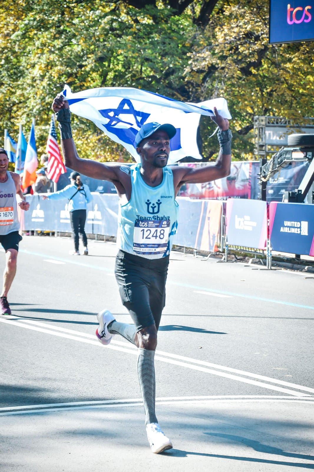 Haimro Alame crossing a marathon finish line holding the Israeli flag above his head.
