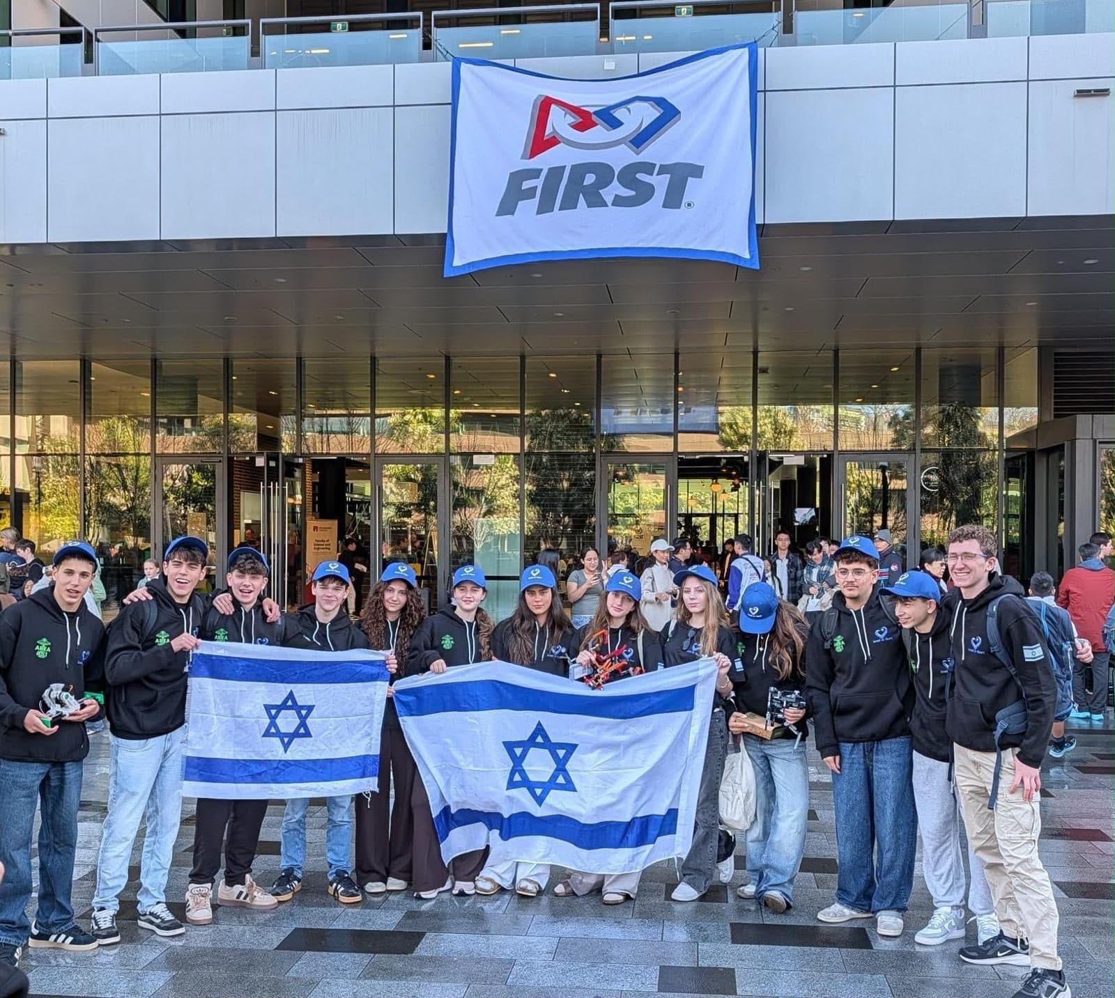 The Handasaim High School robotics team holding Israeli flags beneath the FIRST banner at the championship venue in Sydney.