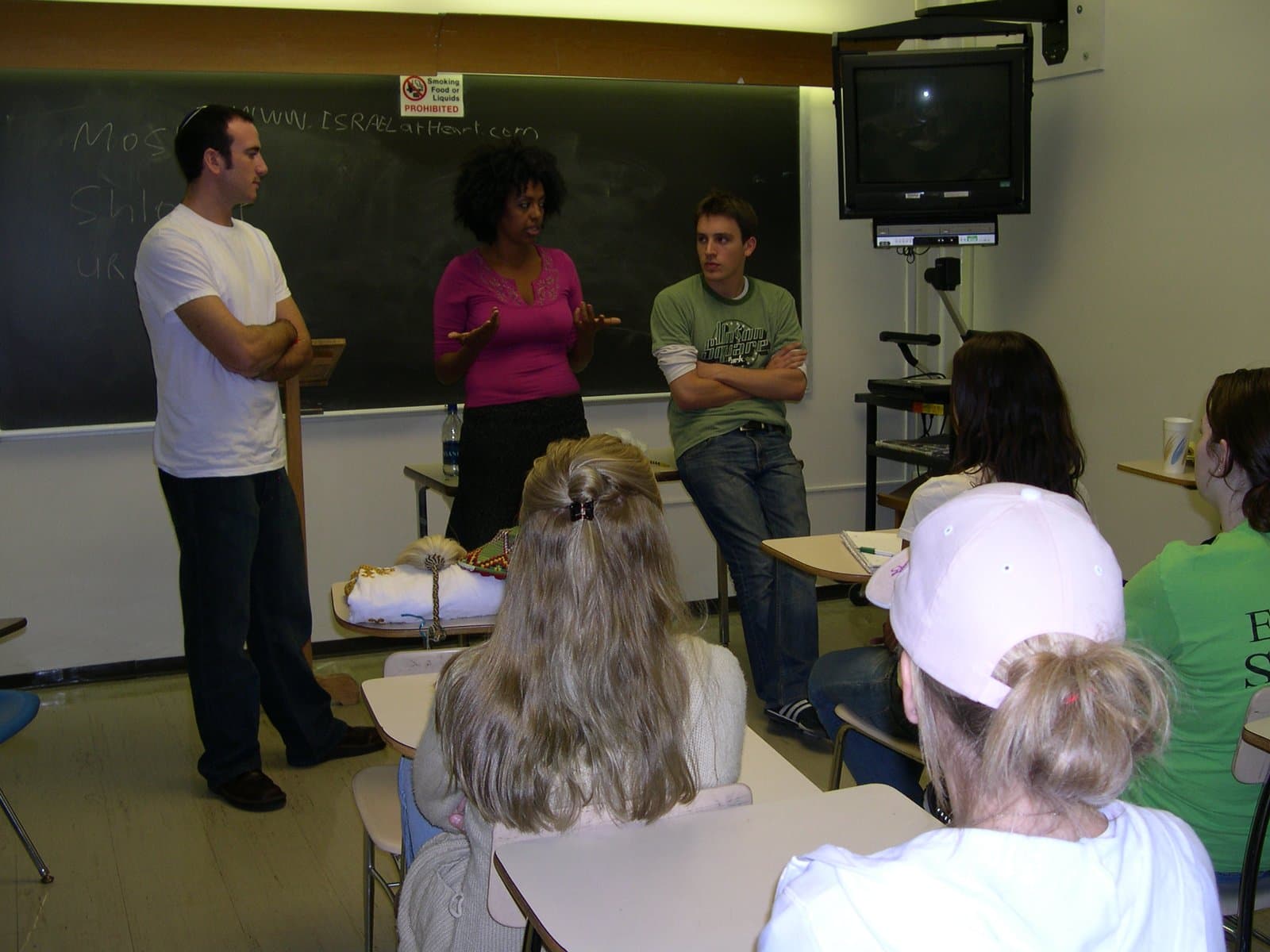 Three Israel at Heart delegates, one of them of Ethiopian origin, speaking with students in a campus classroom.