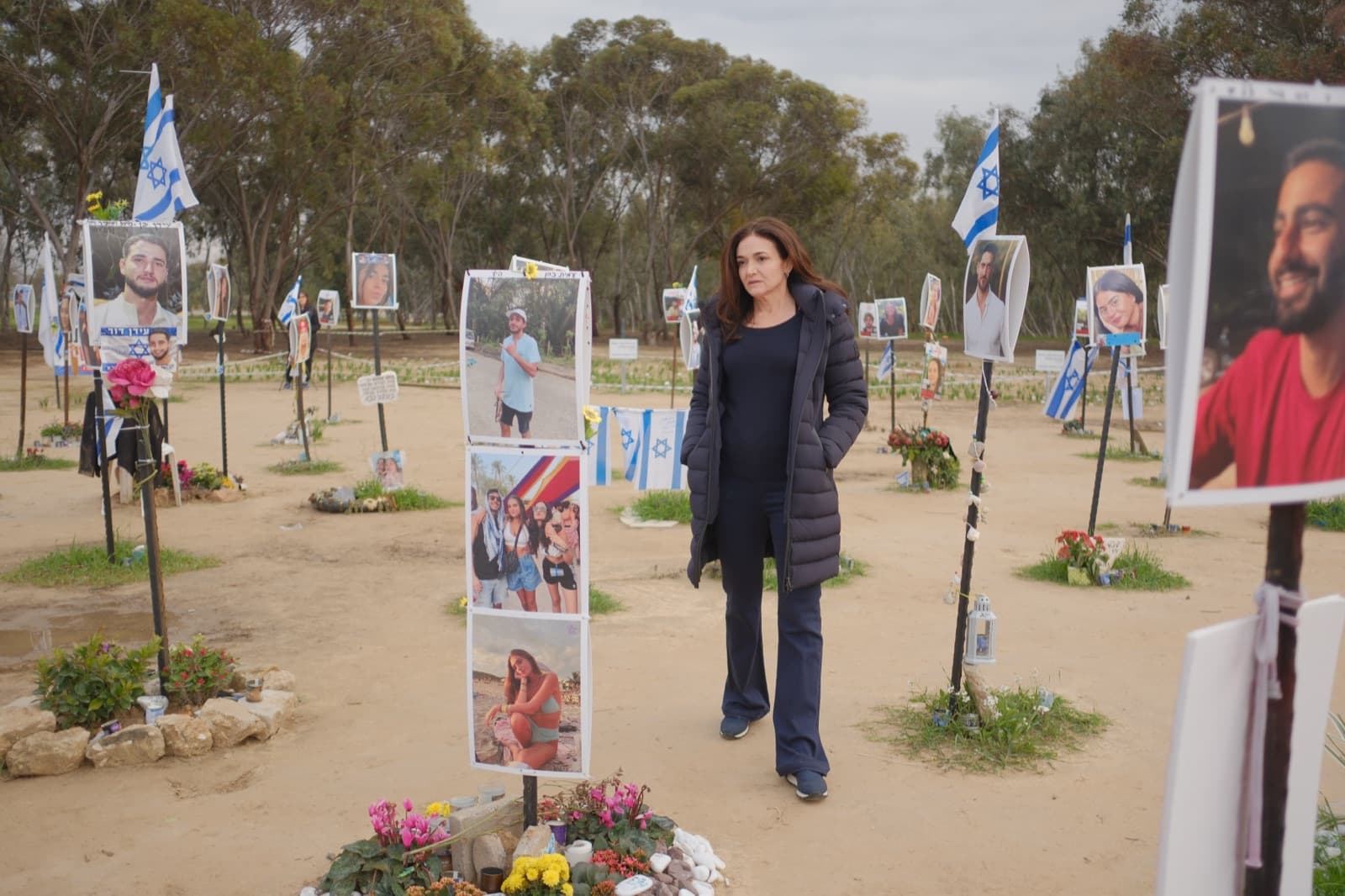 Sheryl Sandberg walking through the memorial at the site of the Nova music festival, portraits of the victims on either side.
