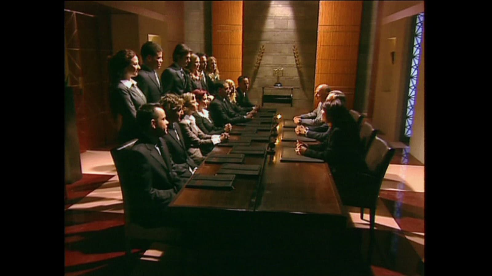 The set of The Ambassador: contestants seated along one side of a long table, facing the judges.