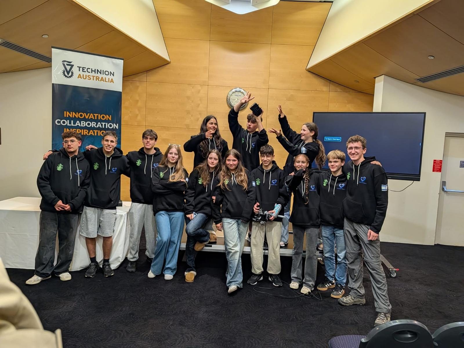 The team gathered beside a Technion Australia banner at the championship in Sydney, one member holding a plaque overhead.